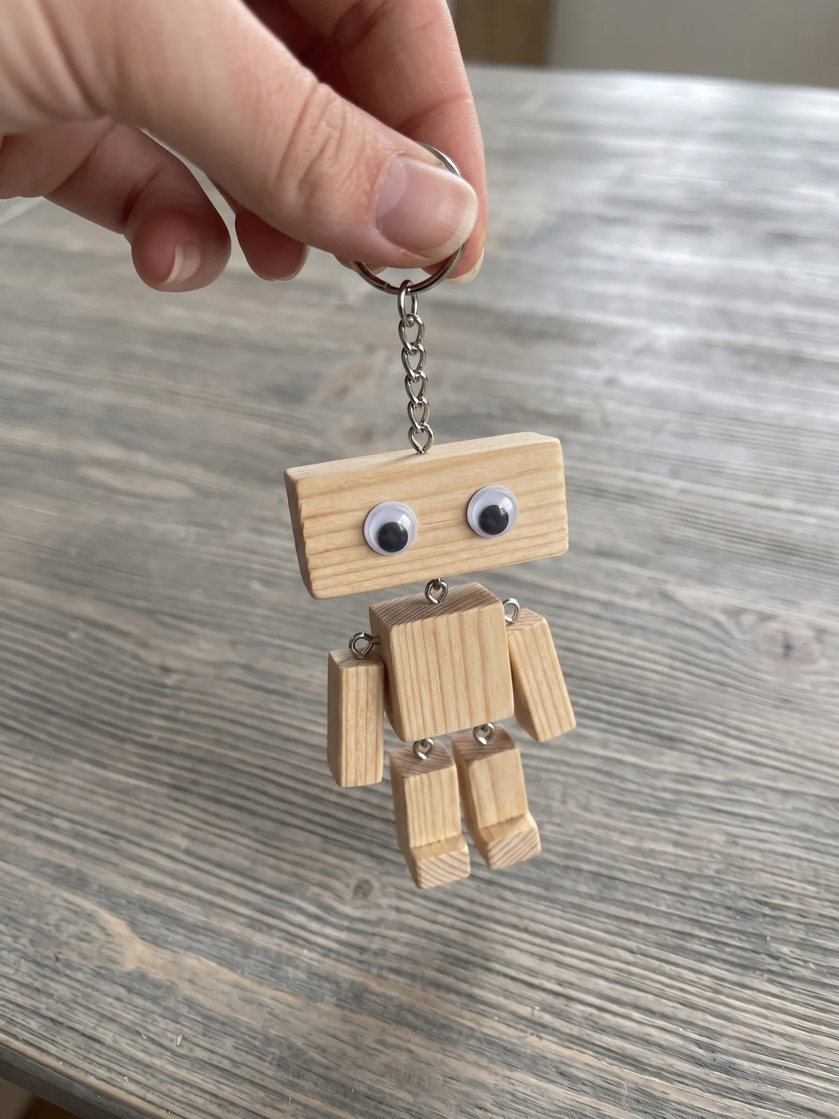 Holzroboter mit Wackelaugen an einem Schlüsselring über grauem Holz