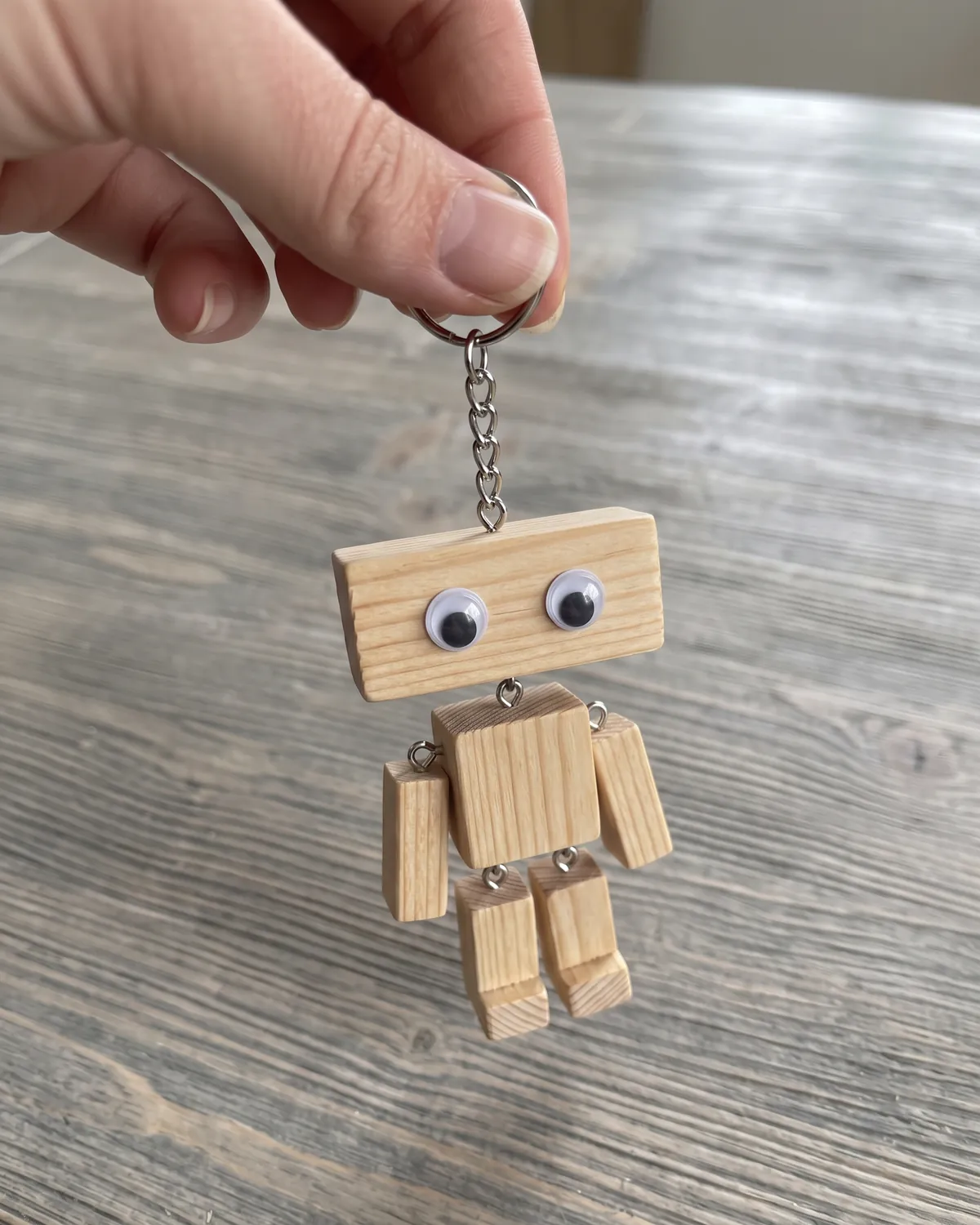 Selbstgemachter Holzroboter als Schlüsselanhänger, an einer Hand baumelnd